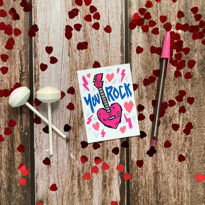 An image of a single classroom Valentine with heart confetti and Valentine’s sweets around it. The design features the words “You rock” with an illustrated heart shaped guitar. 